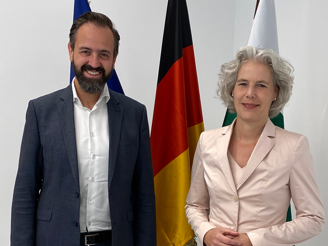 Staatsminister Sebastian Gemkow und Rektorin Prof. Dr. Eva Inés Obergfell vor drei Flaggen.