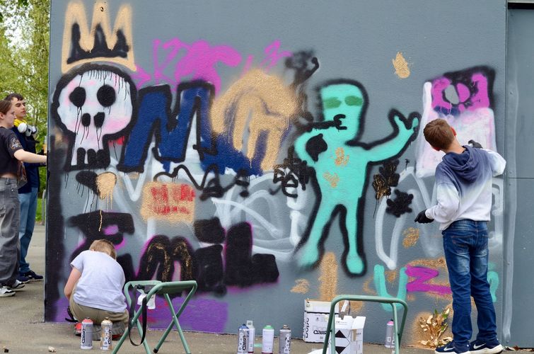 Jugendliche besprühen eine Wand mit Graffiti.