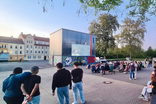 Jüngere und ältere Menschen schauen auf eine Kinoleinwand auf einem Platz in Zeitz.