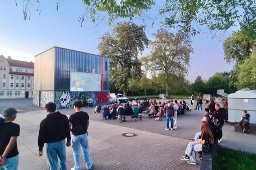 Jüngere und ältere Menschen schauen auf eine Kinoleinwand auf einem Platz in Zeitz.