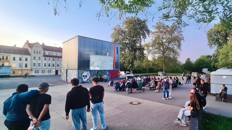 Jüngere und ältere Menschen schauen auf eine Kinoleinwand auf einem Platz in Zeitz.
