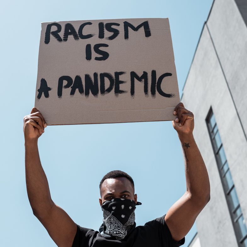 Zu sehen ist ein Demonstrant, der ein Plakat hochhält: "Racism is a Pandemic"