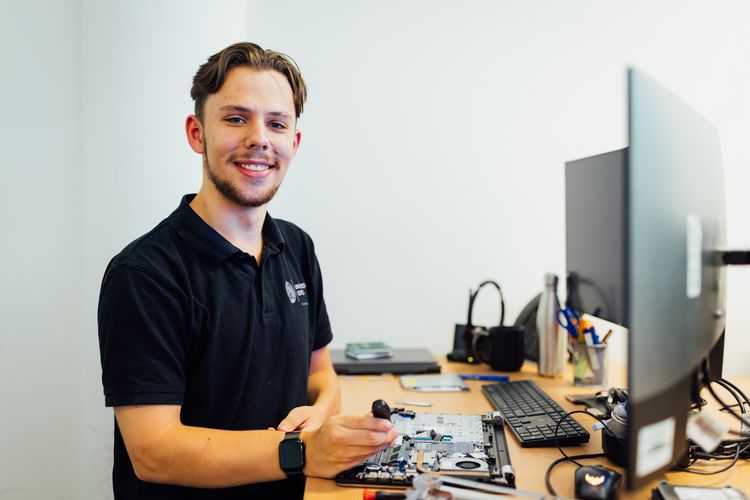 ein Mann steht vor zwei Bildschirmen und schraubt am einem Laptop herum