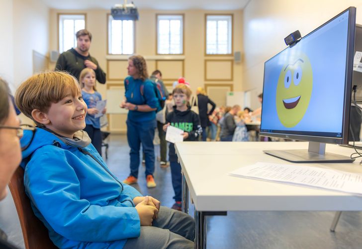 Zu sehen ist ein Kind vor einem Monitor, der einen großen Smiley zeigt.