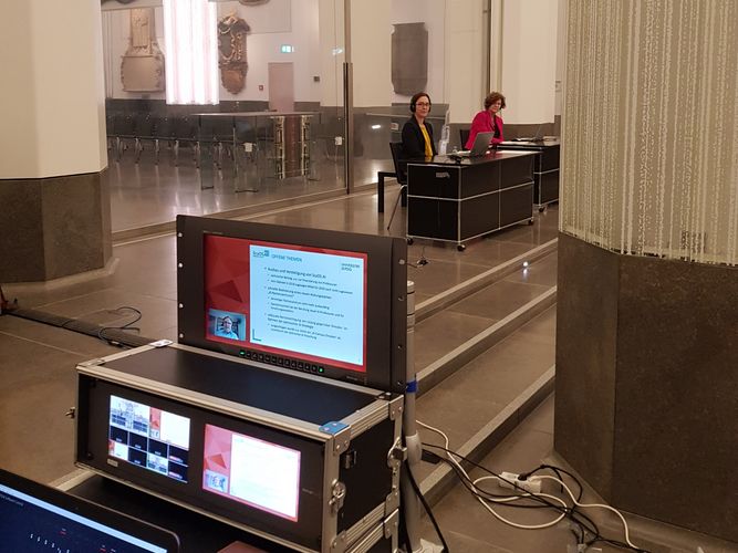 Dr. Claudia Maicher und Rektorin Beate Schücking an einem Redepult im Paulinum, im Vordergrund ein Laptop zur Übertragung des Livestreams.