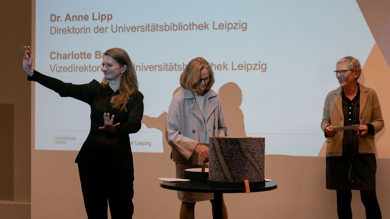 Auf dem Bild sind Caroline Bergter (links), Dr. Anne Lipp (Mitte) und Charlotte Bauer bei der Präsentation der Zeitkapsel beim Jahresempfang der Universitätsbibliothek zu sehen.
