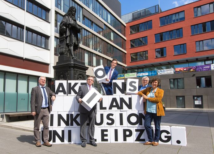 Fünf Personen bauen aus großen weißen Boxen den Schriftzug "Aktionsplan Inklusiuon Uni Leipzig"