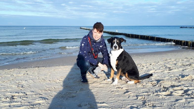 Das Foto zeigt Dekanatssekretärin Ina Scherbaum mit ihrem Hund Filou am Ostseestrand.