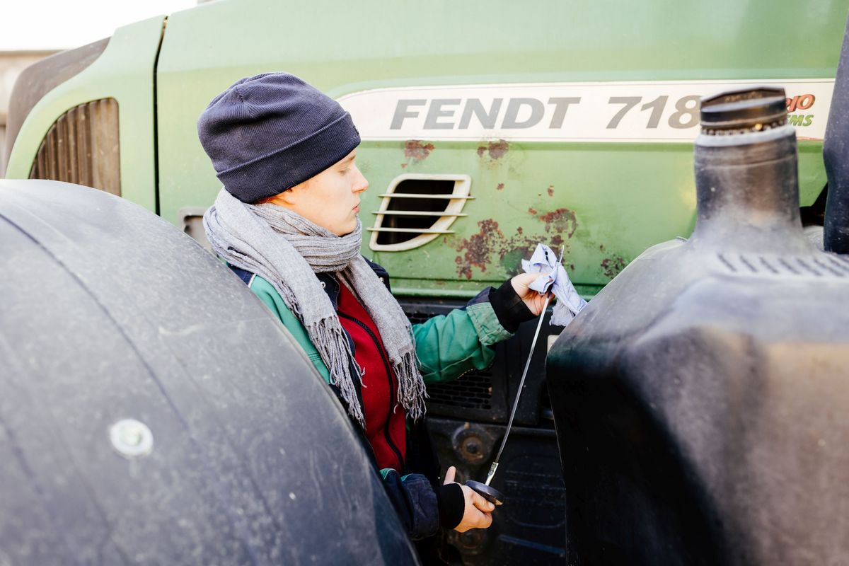 zur Vergrößerungsansicht des Bildes: Mara mit einem Ölmessstab an ihrem Traktor.