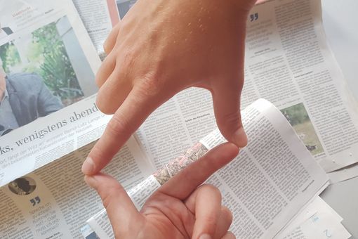 Zwei Hände bilden einen Rahmen über einem Stapel Zeitungen