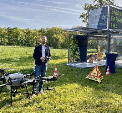 Wirtschaftsinformatiker Martin Schieck überprüft die Drohne nach ihrem Flug übers Versuchsfeld. Foto: Diana Smikalla Auf dem Bild ist Wirtschaftsinformatiker Martin Schieck auf einer Wiese neben einer Drohne zu sehen. Neben ihm das Smart Farming Lab.ersuchsfeld. Foto: Diana Smikalla