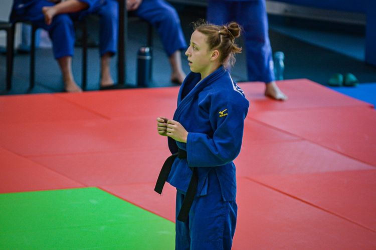 Frau im blauen Kampfsportanzug steht mit dem Profil allein im Bild.