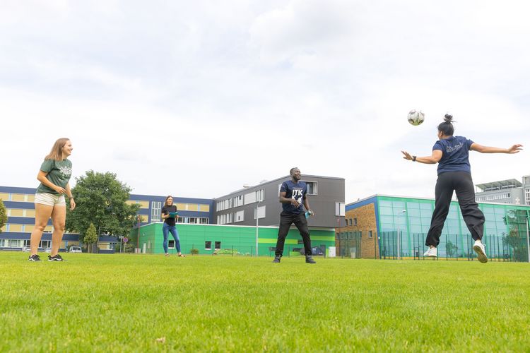 Auf dem Bild sind Yamuna, Brian und Mariana beim gemeinsamen Fußballtaining auf der Leichtathletikanlage der Sportwissenschaftlichen Fakultät. Sie üben präzise Kopfbälle. 