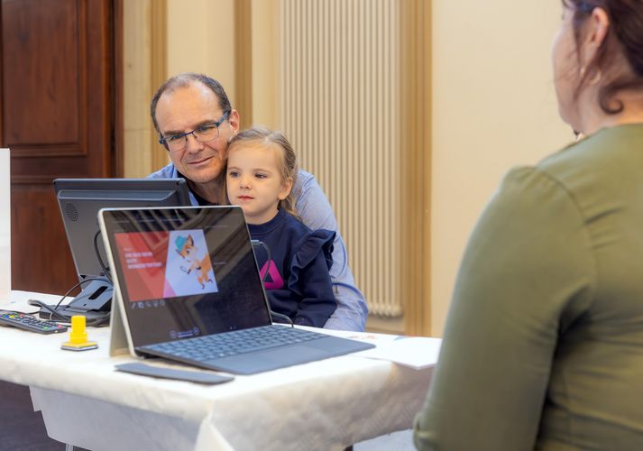 Zu sehen ist ein Vater mit seinem Kind vor einem Computerbildschirm.