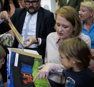 Auf dem Bild schauen sich Bundesfamilienministerin Lisa Paus und Sachsens Kultusminister Christian Piwarz - umringt von Kindern - Bilder der Kleinen an.