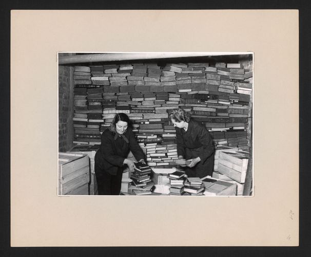Zu sehen sind zwei Mitarbeiterinnen beim Einpacken von Büchern in Kisten.