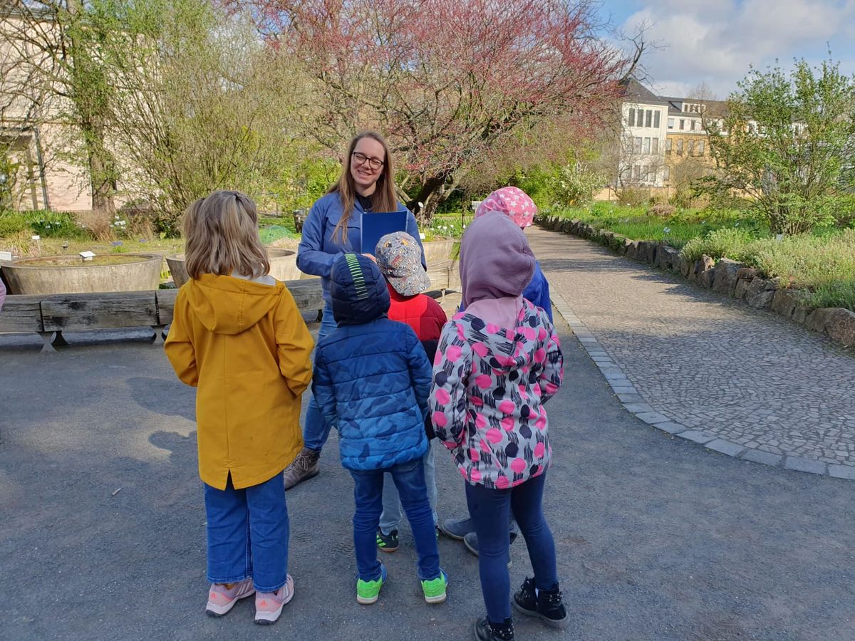 zur Vergrößerungsansicht des Bildes: Zu sehen ist Franciska Frese, wie sie ihrer Grundschulklasse im Botanischen Garten Dinge erklärt.