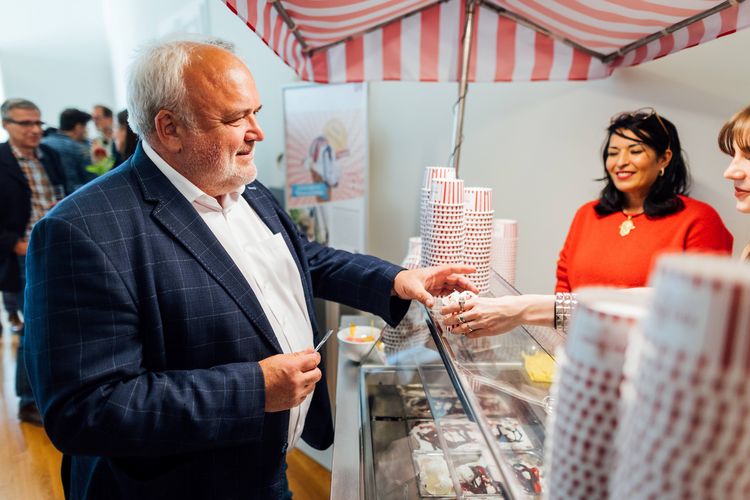 Jörg Junhold steht an einem Eisstand und bekommt über den Tresen ein Eis gereicht.