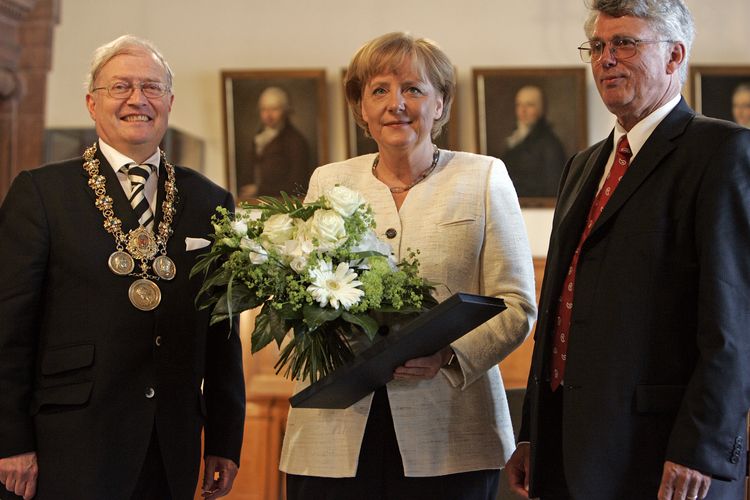 Das Bild zeigt Angela Merkel bei der Verleihung der Ehrendoktorwürde. Auf dem Bild sind auch der damaligen Dekan der Fakultät für Physik und Geowissenschaften, Prof. Dr. Tilman Butz und der damaligen Rektor der Universität Leipzig, Prof. Dr. Franz Häuser, zu sehen.