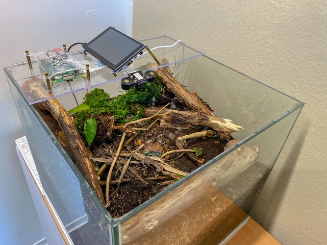 Terrarium gefüllt mit Holz und Erde, darüber technische Geräte