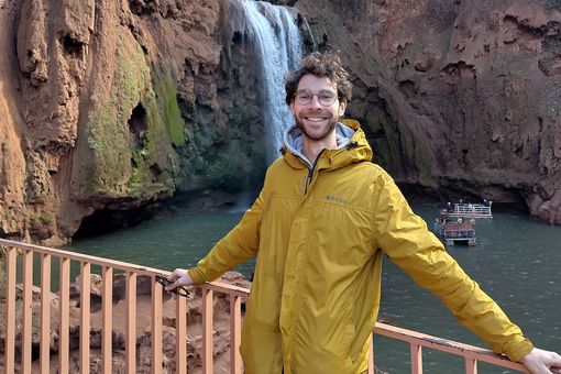 Zu sehen ist Max Schmidt, im Hintergrund zu sehen ist eine Felsenwand mit einem Wasserfall. 