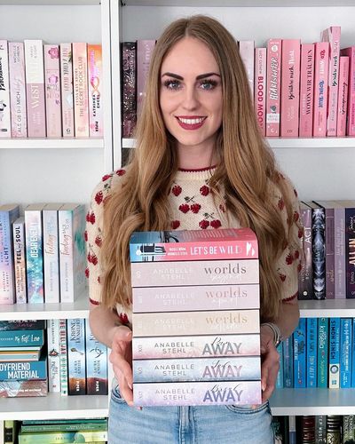 Anabelle Stehl mit einem Stapel Bücher vor ihrem Bücherregal
