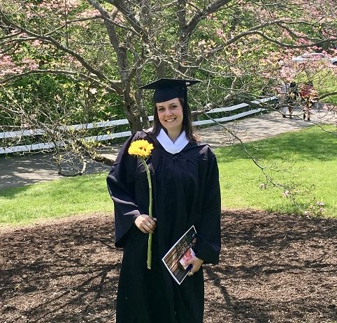 Zu sehen ist Cosima Hummel im Talar nach ihrer Graduierung in einem Park unter einekm blühenden Baum.