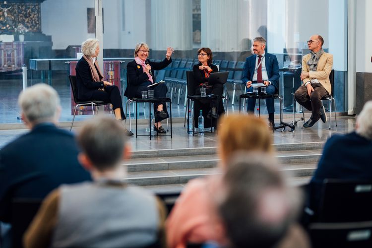 Zu sehen ist eine Diskussionsgruppe auf der Bühne, sie besteht aus fünf Menschen.