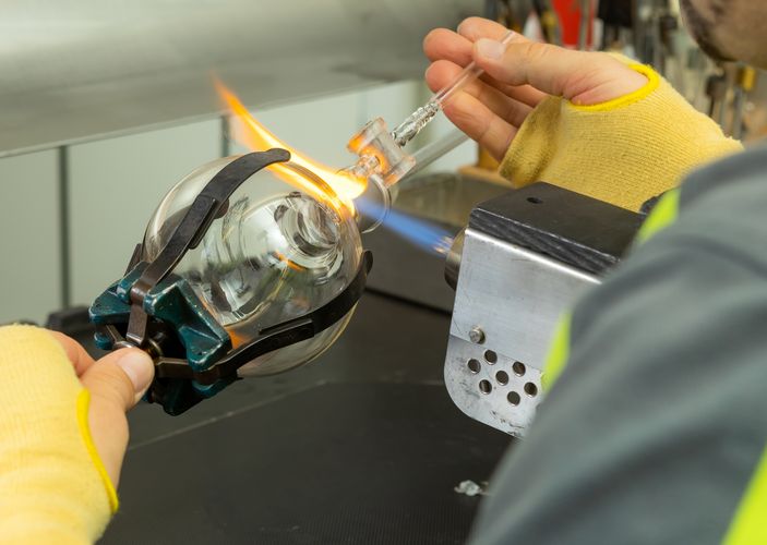Mit kleinerer Flamme wird Glas erhitzt, um verschiedene Bauteile milimetergenau miteinander zu verschmelzen.